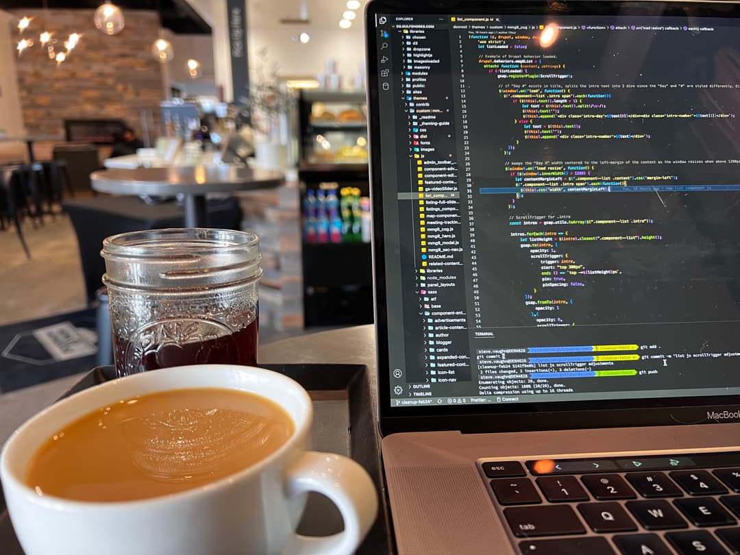 A laptop open with code on the screen, with a cup of coffee next to the laptop