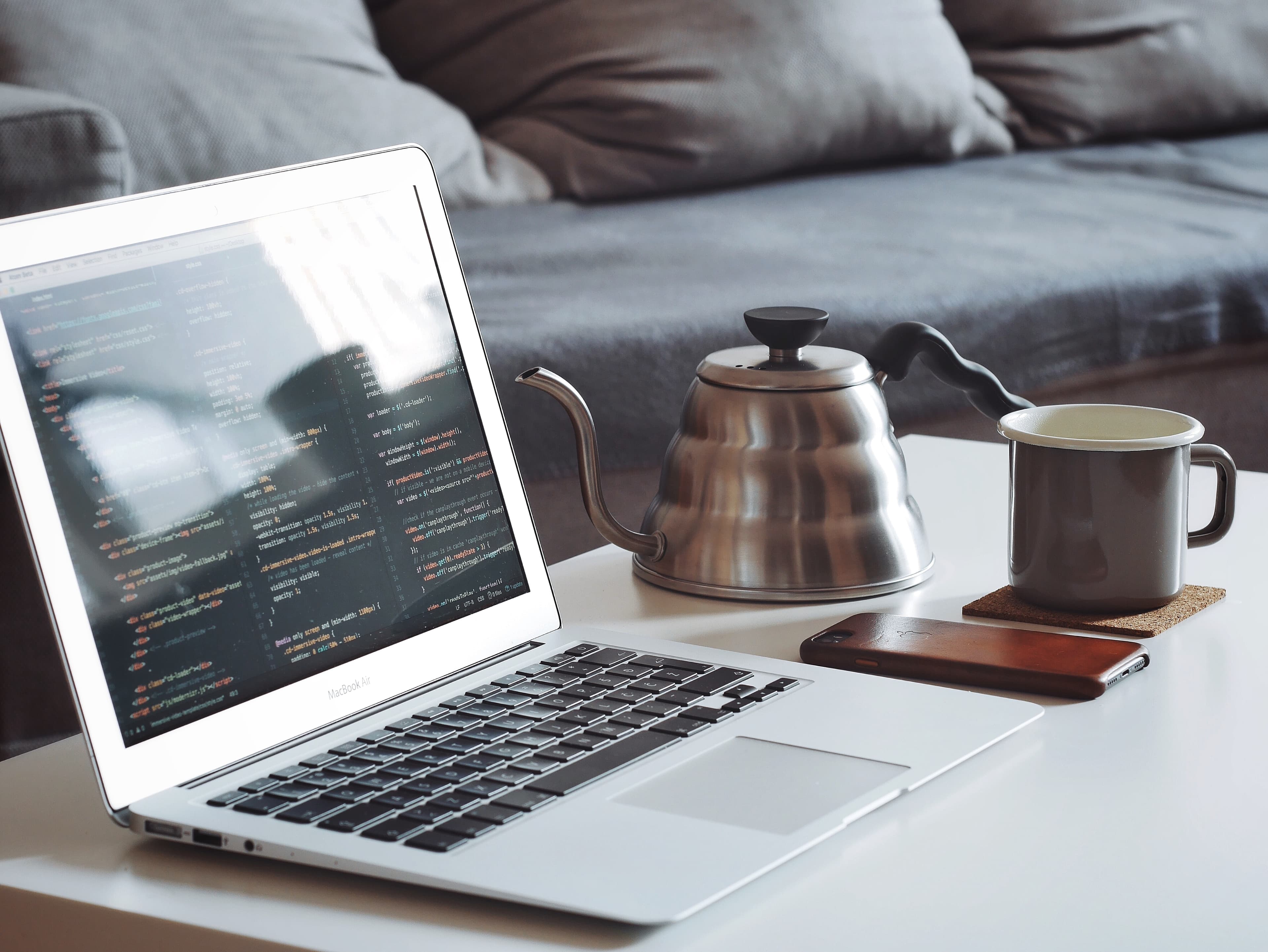 Turned on MacBook Air beside black smartphone and black ceramic mug